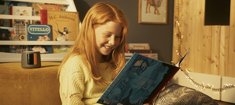 young girl reading a book with TUK speaker in the background
